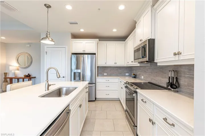 Kitchen featuring stainless steel appliances, white cabinets, hanging light fixtures, light tile patterned floors & light stone countertops