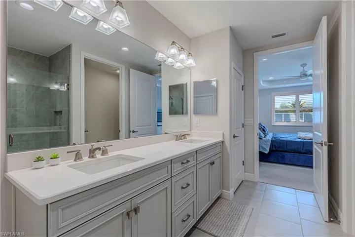 Bathroom featuring double vanity, ensuite bathroom, shower stall, light tile patterned floors & ceiling fan