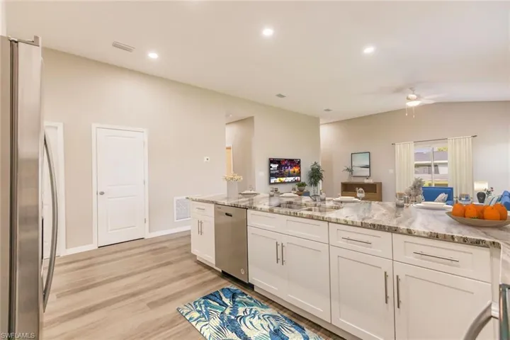 Kitchen with stainless steel appliances, light stone counters, ceiling fan, white cabinetry, and light wood finished floors