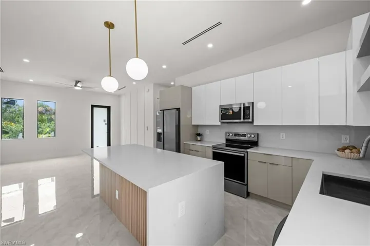 Modern kitchen featuring a waterfall island with wood slat detail, polished tile flooring, white flat-panel cabinetry, stainless steel appliances, and pendant lighting