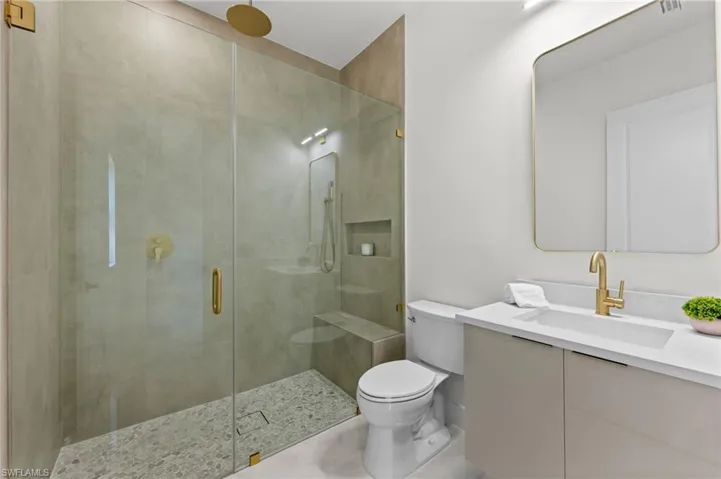 Contemporary bathroom featuring a frameless glass shower enclosure with gold-tone fixtures, a built-in shower bench, and pebble tile flooring