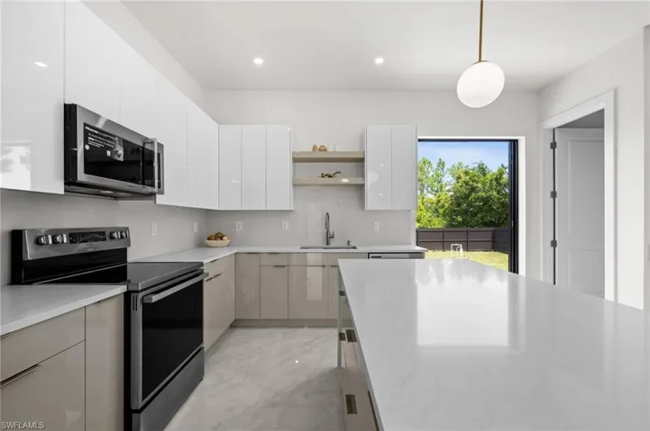 Modern kitchen featuring a large central island with a light-toned countertop, stainless steel appliances, gloss-finish cabinetry, a built-in microwave, and a glass door leading to the backyard