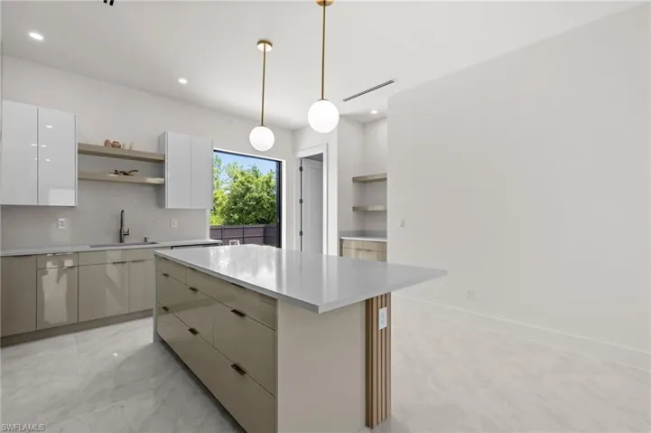 Modern kitchen featuring a spacious center island with a light-toned countertop, sleek cabinetry with an integrated sink, polished tile flooring, pendant lighting fixtures, and open shelving