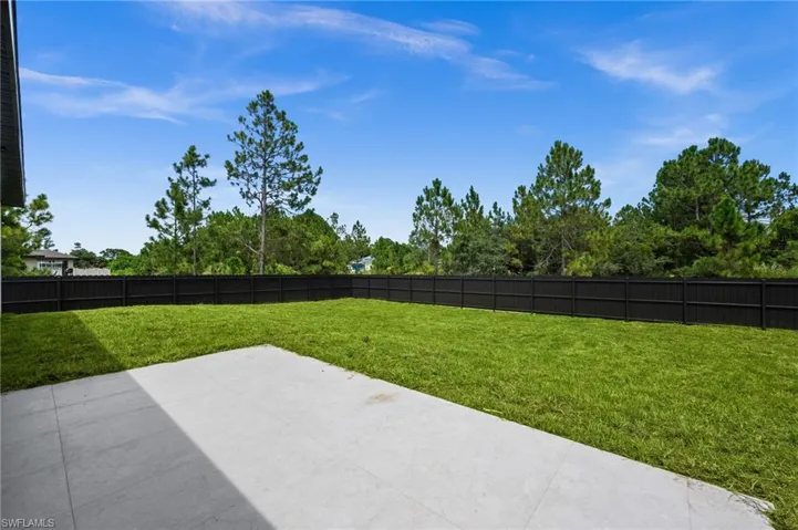 Expansive backyard featuring a manicured lawn, a concrete patio, and a dark privacy fence
