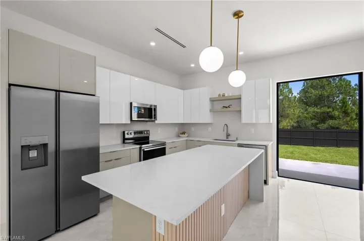 Modern kitchen featuring a spacious island with a light countertop, stainless steel appliances, white and gray cabinetry, and a sliding glass door opening to a private backyard