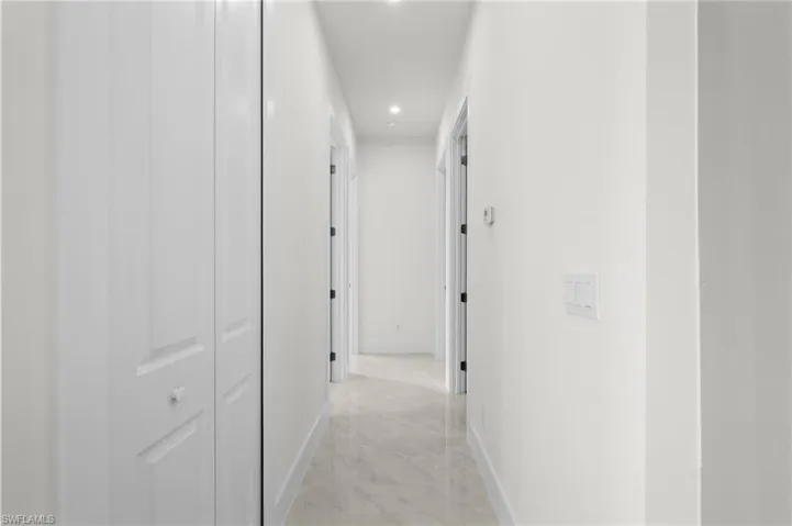 Bright hallway featuring clean white walls, recessed lighting, and light-toned tile flooring