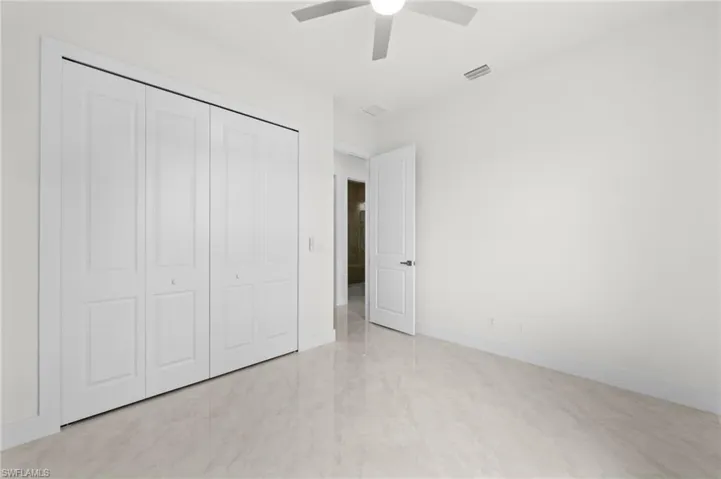 Bright room featuring a ceiling fan, white paneled bifold closet doors, a white paneled door, and large format tile flooring