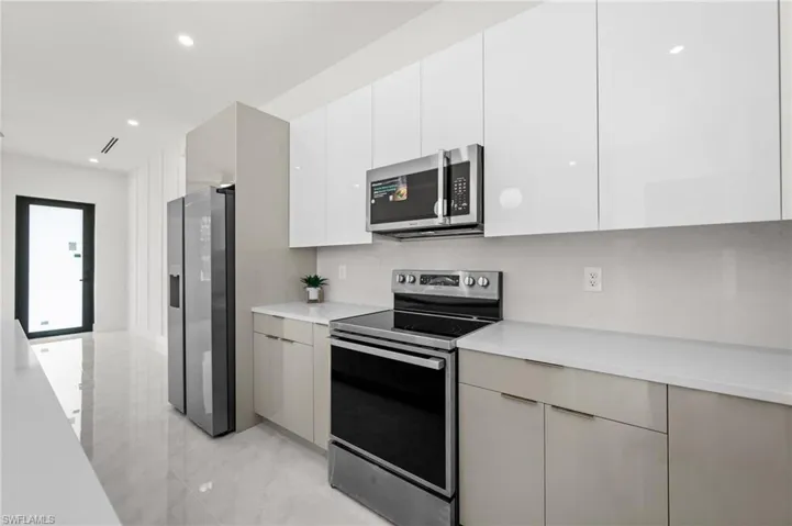 Modern kitchen featuring white glossy upper cabinetry, light gray base cabinetry, stainless steel appliances, and white countertops