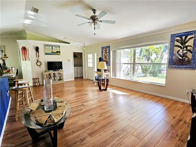 Living room with ceiling fan, ornamental molding, vaulted ceiling, and light wood-type flooring