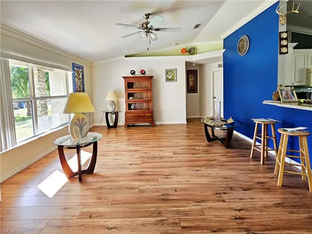 Living area with crown molding, light hardwood / wood-style flooring, ceiling fan, and vaulted ceiling