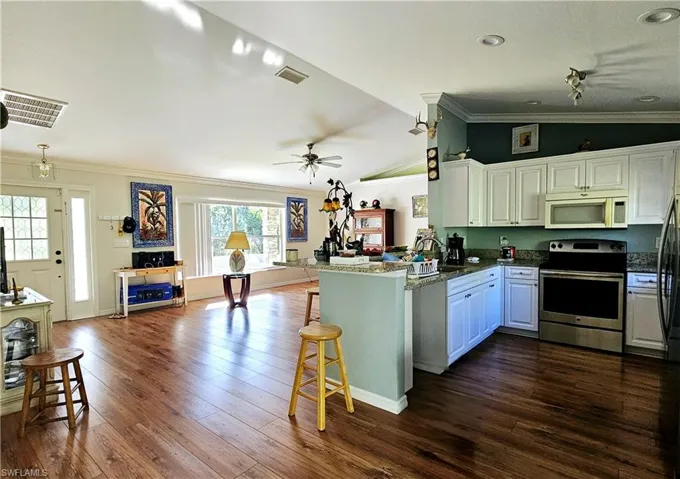 Kitchen with white cabinetry, stainless steel appliances, kitchen peninsula, vaulted ceiling, and ornamental molding