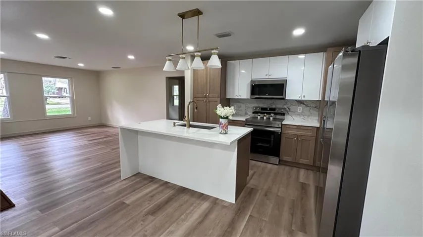 Kitchen featuring stainless steel appliances, dual tone cabinets, open floor plan, an island with sink, and light wood-style floors