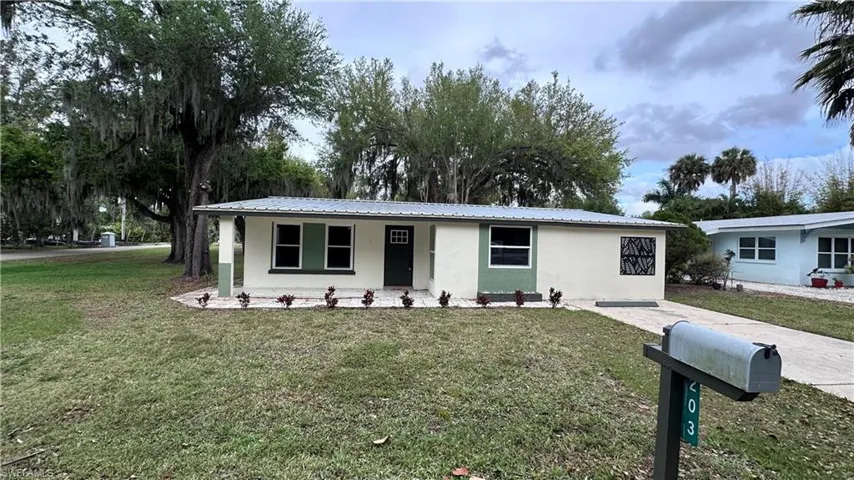 Ranch-style home featuring stucco siding, a front yard, covered porch, and a metal roof