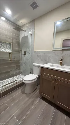Full bath featuring vanity, a stall shower, tile walls, and wood tiled floors