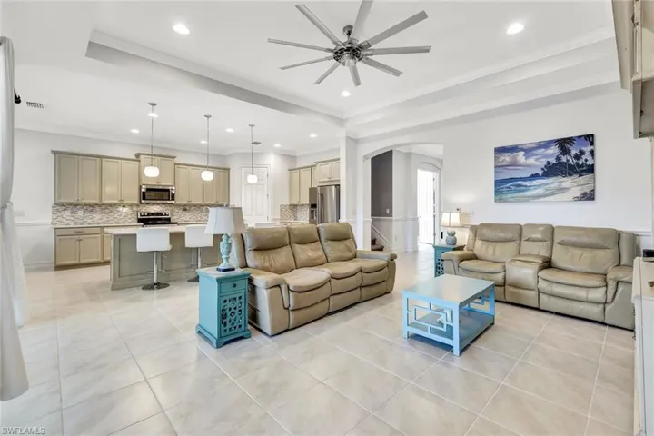 Living area with ornamental molding, arched walkways, ceiling fan, and light tile patterned floors