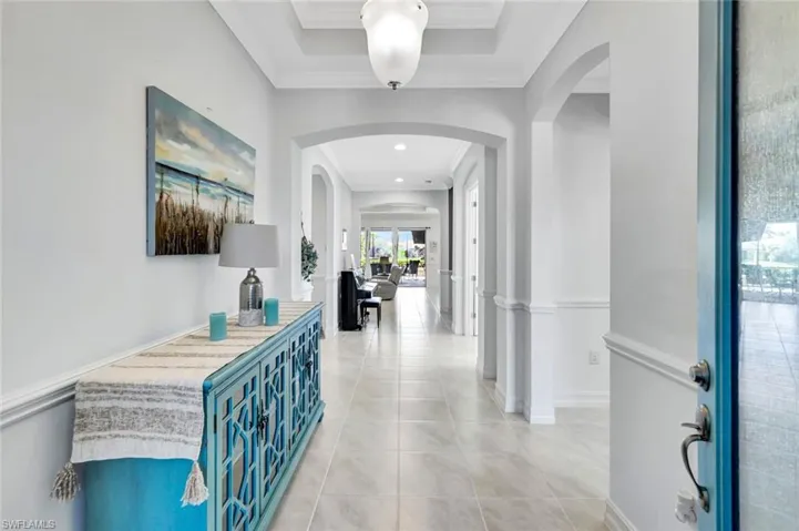 Corridor with arched walkways, crown molding, baseboards, and light tile patterned floors