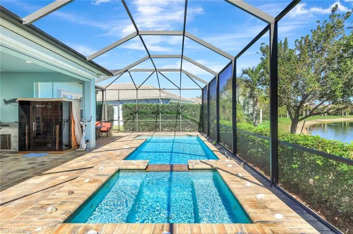 View of pool featuring glass enclosure, a pool with connected hot tub, a patio area, and a water view