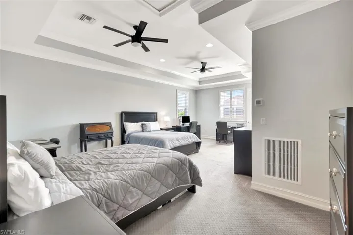 Bedroom with light carpet, a tray ceiling, visible vents, and crown molding
