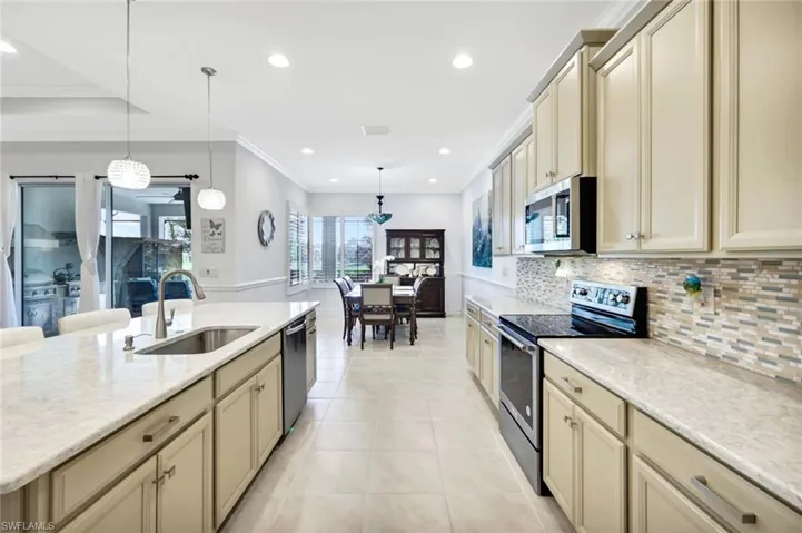 Kitchen with light tile patterned floors, stainless steel appliances, a sink, cream cabinetry, and backsplash