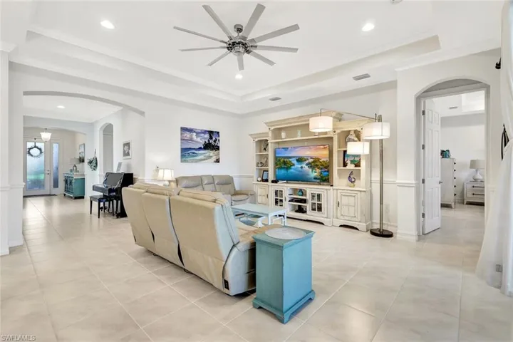 Living area featuring light tile patterned floors, a tray ceiling, arched walkways, and ornamental molding