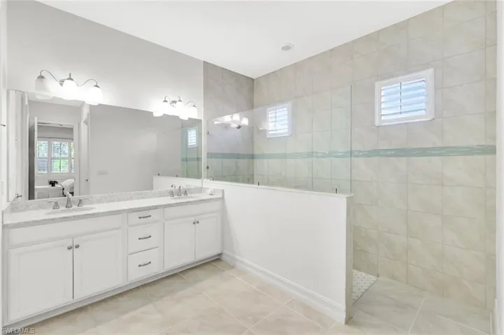 Bathroom featuring a walk in shower, double vanity, ensuite bath, and a sink
