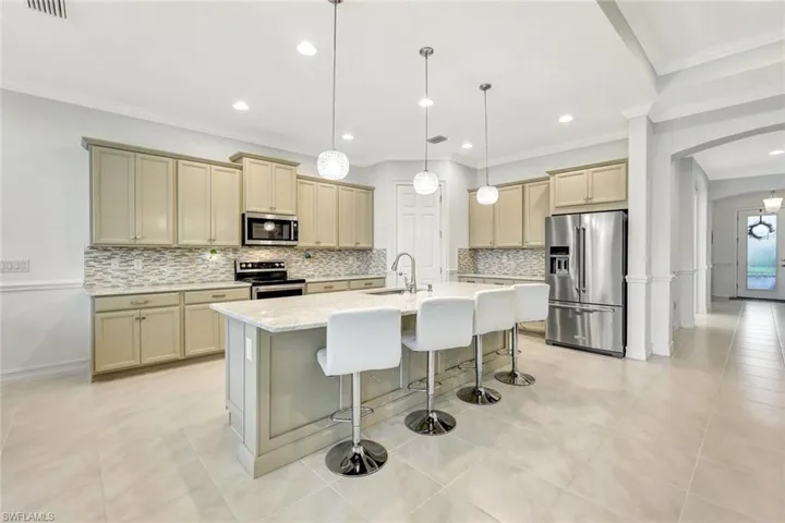 Kitchen with tasteful backsplash, a center island with sink, arched walkways, appliances with stainless steel finishes, and a kitchen breakfast bar
