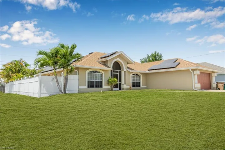 View of front of house with roof mounted solar panels, an attached garage, a front lawn, and stucco siding