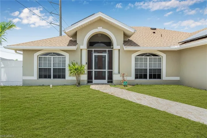 Entrance to property with a yard, roof with shingles, and stucco siding