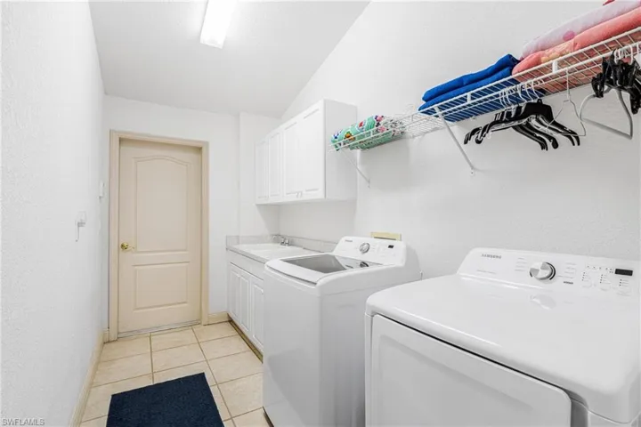 Clothes washing area with a sink, light tile patterned floors, washer and dryer, cabinet space, and baseboards