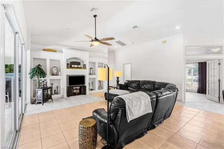 Living room with a ceiling fan, light tile patterned floors, light carpet, a wood stove, and built in features