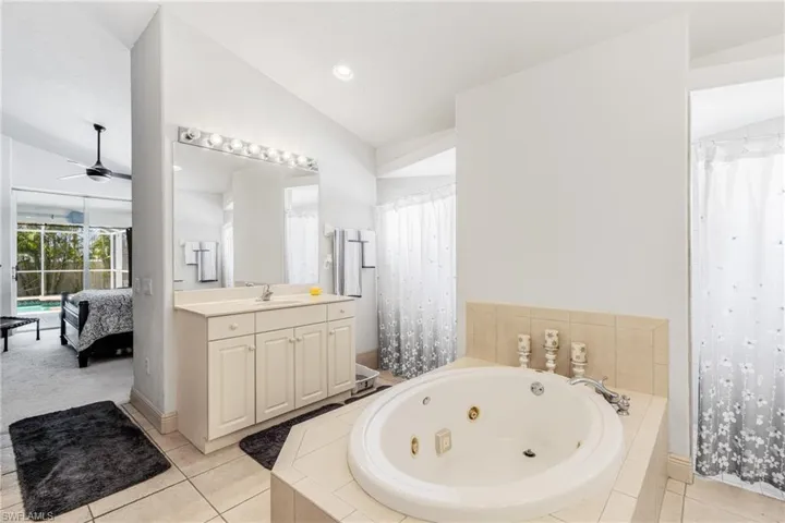 Bathroom featuring ensuite bathroom, lofted ceiling, a whirlpool tub, ceiling fan, and vanity