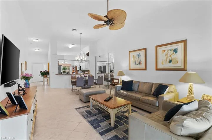 Tiled living room with high vaulted ceiling and ceiling fan with notable chandelier