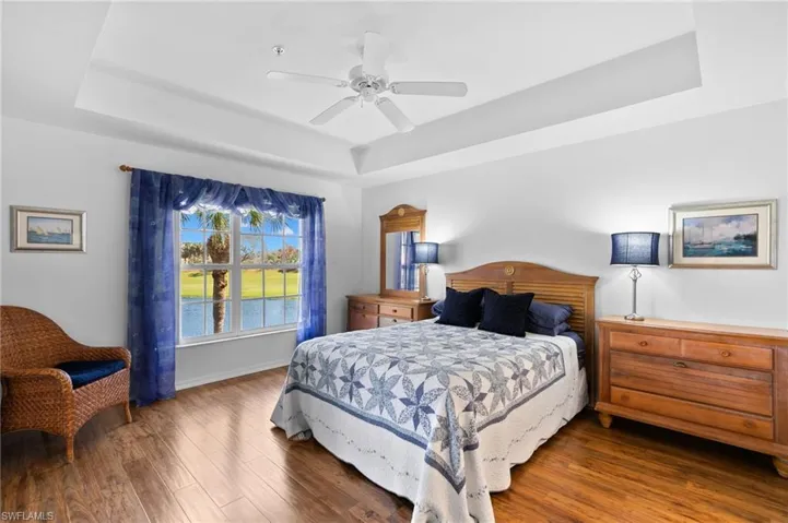 Bedroom with dark hardwood / wood-style floors, a tray ceiling, and ceiling fan