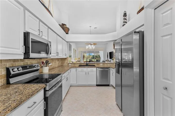 Kitchen with an inviting chandelier, appliances with stainless steel finishes, white cabinetry, and dark stone countertops