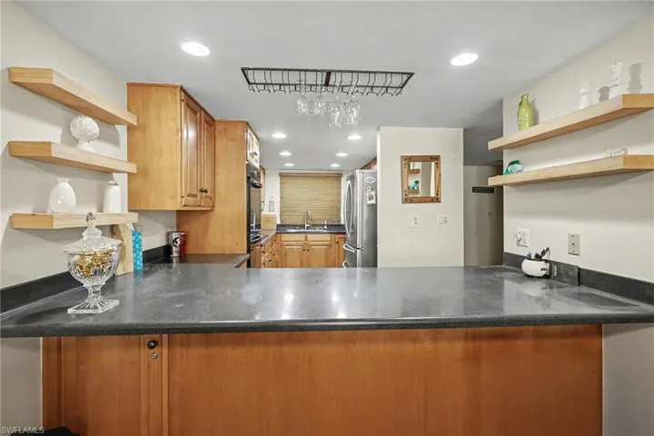 Kitchen with open shelves, recessed lighting, freestanding refrigerator, wood finish cabinets, and dark stone counters