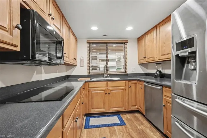 Kitchen featuring black appliances, dark countertops, light wood-type flooring, and recessed lighting
