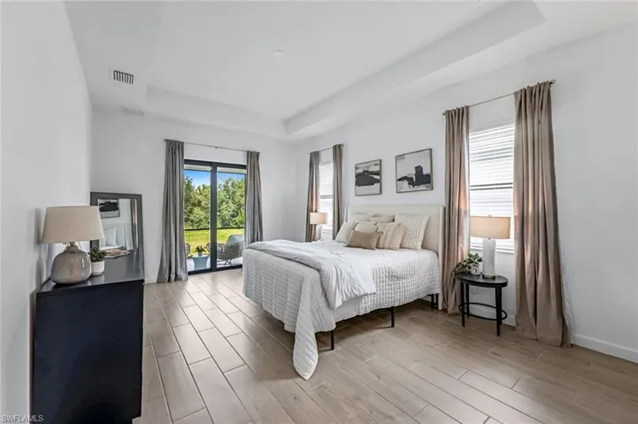 Bedroom featuring access to outside, wood-type flooring, and a raised ceiling
