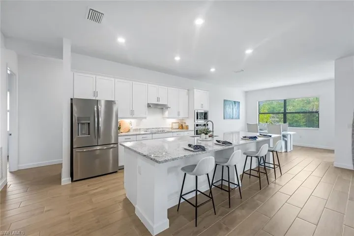 Kitchen with light hardwood / wood-style floors, a kitchen island with sink, a breakfast bar area, white cabinetry, and appliances with stainless steel finishes