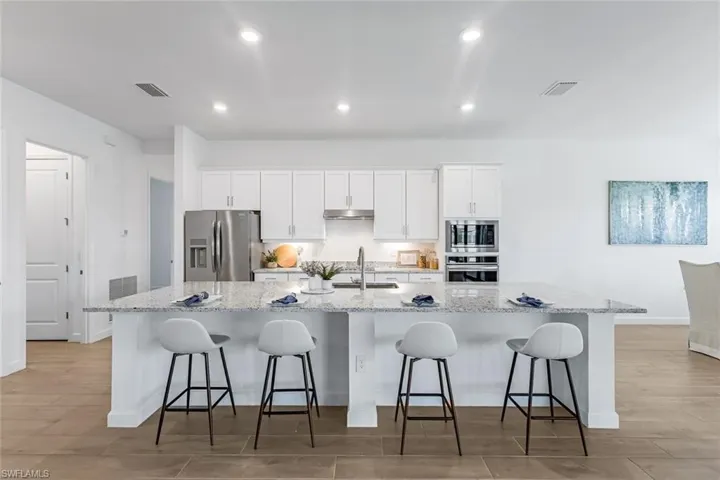 Kitchen with light hardwood / wood-style floors, white cabinets, sink, a large island, and appliances with stainless steel finishes