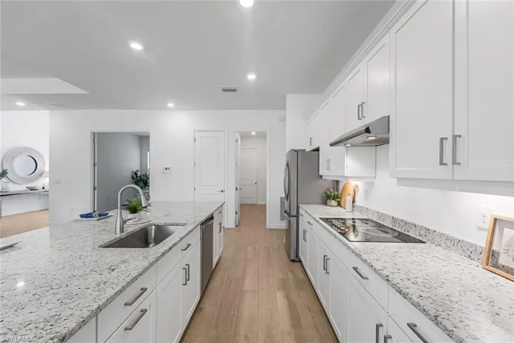 Kitchen with light stone countertops, light hardwood / wood-style flooring, black electric cooktop, sink, and white cabinetry