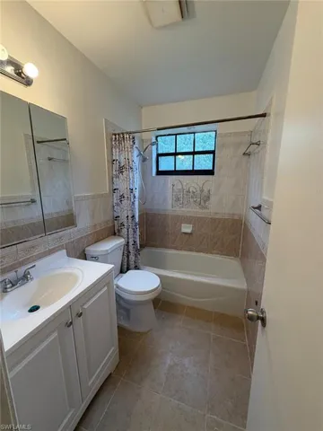 Full bathroom featuring a white vanity with integrated sink, tiled flooring, a bathtub with shower fixture, and a window with privacy glass