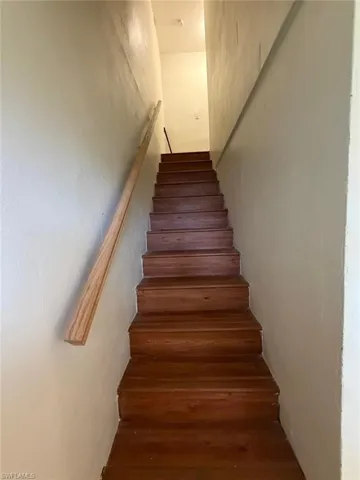 Staircase featuring wood-finish treads and risers, a light-toned wood handrail, and light-colored walls