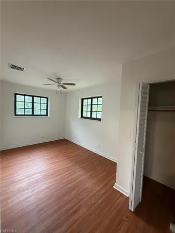 Spacious room featuring wood-finish flooring, two windows with black frames, a ceiling fan, and white painted walls