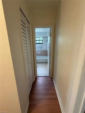 Hallway featuring wood-finish flooring, light neutral wall paint, and louvered bifold closet doors