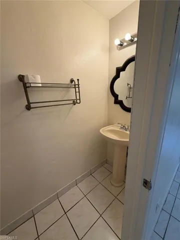 Pedestal sink with chrome faucet, complemented by a decorative mirror and vanity lighting