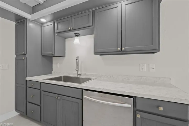 Kitchen with stainless steel dishwasher, gray cabinetry, and light countertops