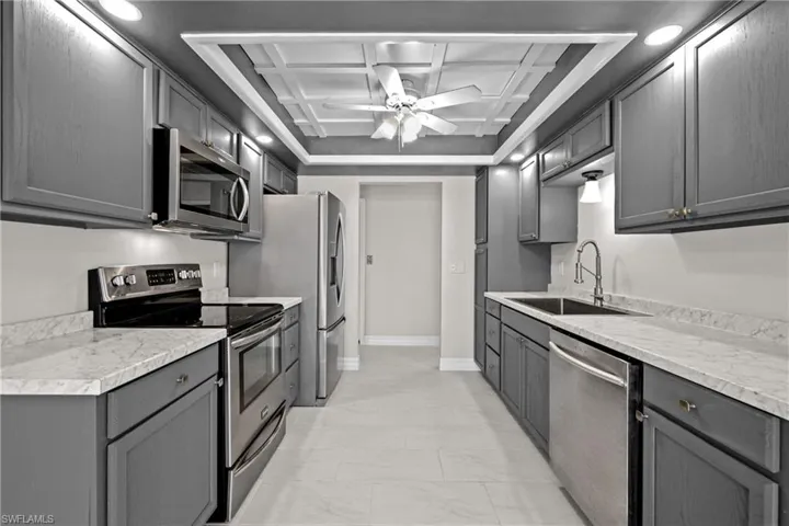 Kitchen with appliances with stainless steel finishes, light marble finish flooring, coffered ceiling, a ceiling fan, and gray cabinetry