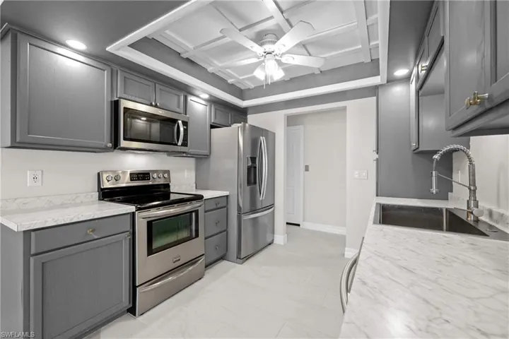 Kitchen with appliances with stainless steel finishes, coffered ceiling, ceiling fan, and gray cabinets