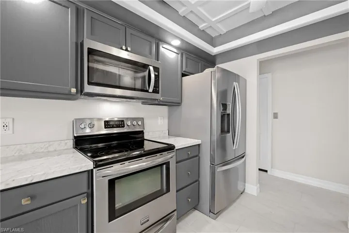 Kitchen with appliances with stainless steel finishes, gray cabinets, light stone countertops, and coffered ceiling