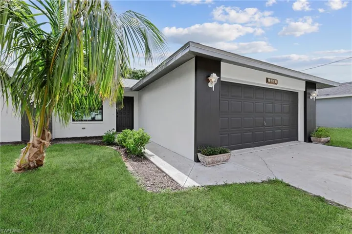 View of front facade featuring a garage, driveway, a front yard, and stucco siding